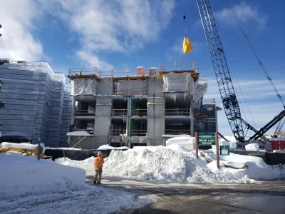 Deer Valley condos under construction in winter with snow, crane, and worker on site