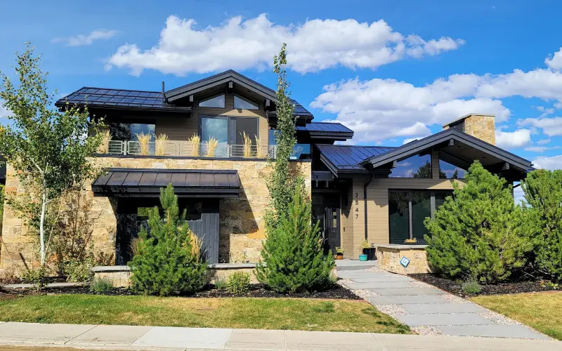Contemporary luxury home exterior in Aspen Springs Ranch, Park City, Utah, with natural stone masonry, solar panels, and mature landscaping