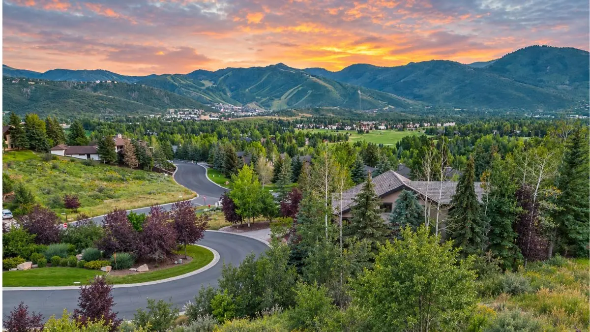 Homes along a tree-lined street in Park Meadows, Park City, UT 84060, with the ski resorts on the skyline at sunset