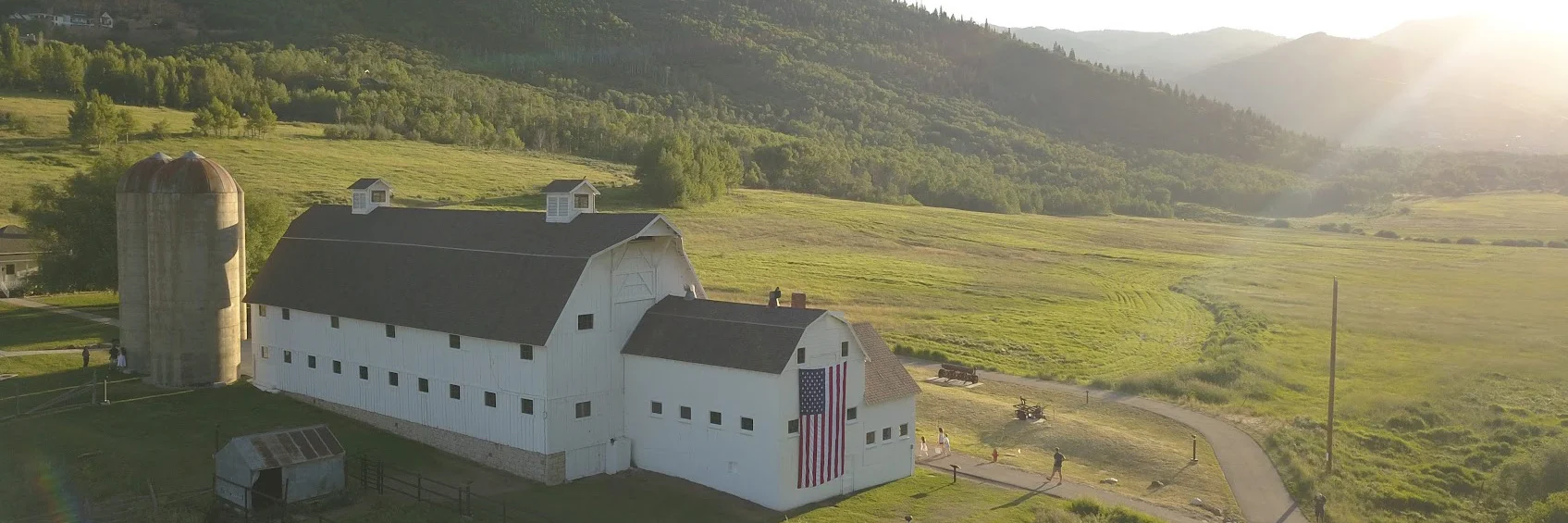 Aerial view of the historic white McPolin Barn near Aspen Springs Ranch in Park City, Utah, with mountain landscape and open fields in the background