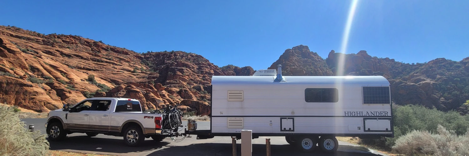White Ford truck towing a Highlander RV trailer through Utah red rock canyons, symbolizing outdoor living and RV-friendly homes in Park City.