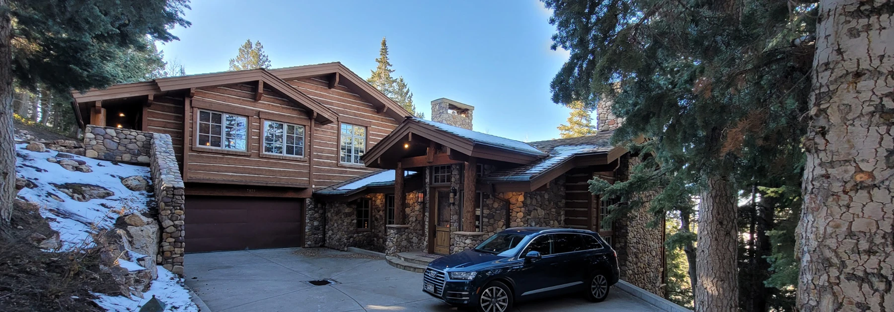 Luxury log and stone home in Upper Deer Valley surrounded by pine trees and snow in Park City, Utah